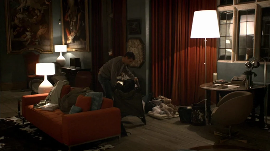 A Cock and Bull Story (2005) movie still: wide — A spacious room features high ceilings, dark walls, and large oil paintings. A man is assembling a…