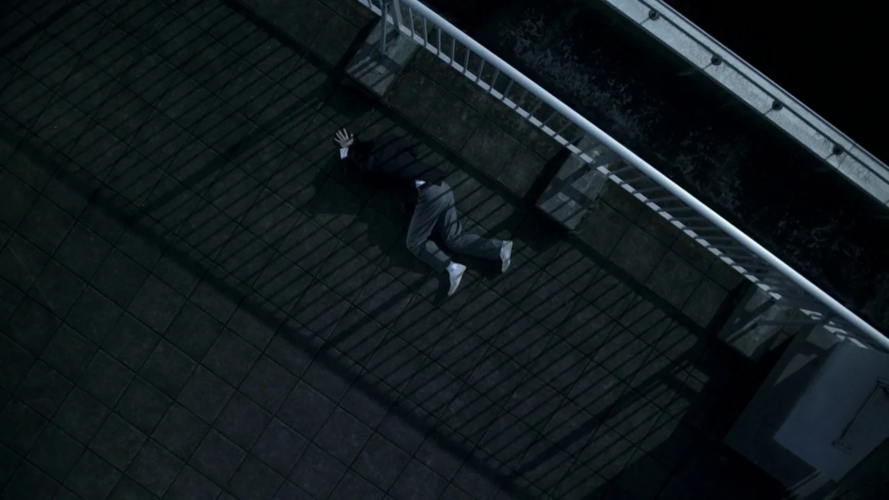 Confessions (2010) movie still: wide — A dark, paved walkway beside a white metal railing at night. A person in a dark suit lies prostrate on the…