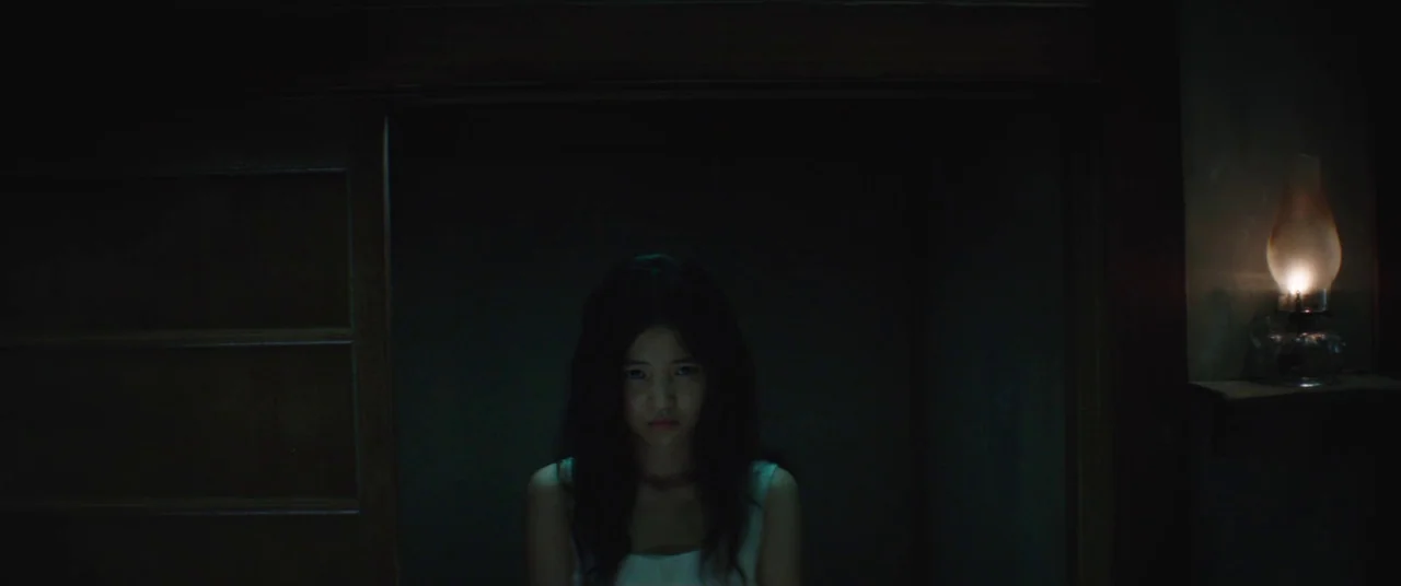 The Handmaiden (2016) movie still: medium — A dimly lit room with dark walls features a single shelf on the left. A young woman sits in the center…