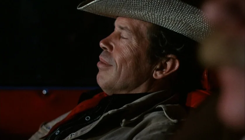 Cockfighter (1974) movie still: closeup — The interior of a vehicle at night with dark shadows surrounding the subject. A mature man in a straw…