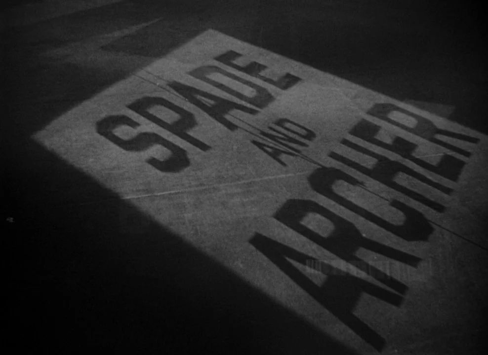 The Maltese Falcon (1941) movie still: closeup — The words Spade and Archer are stenciled in sharp shadows upon a wooden door. Light filters through…