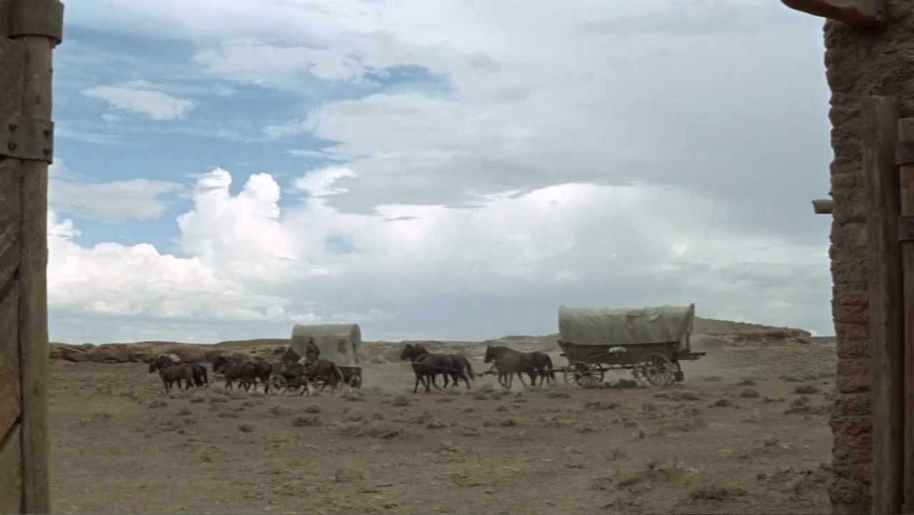 A Distant Trumpet (1964) movie still: wide — An open desert landscape is framed by two adobe walls on the sides. Two horse-drawn covered wagons…