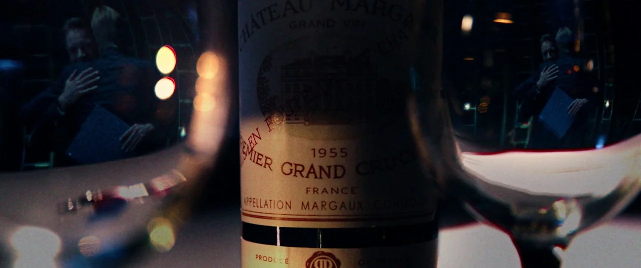 Steve Jobs (2015) movie still: closeup — A close-up shot focuses on a vintage 1955 Chateau Margaux wine bottle label. Blurred figures reflect within…