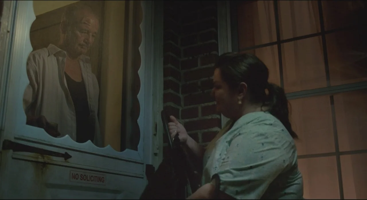 St. Vincent (2014) movie still: medium — An exterior residential porch at night features a man behind a white screen door. A woman stands in the…
