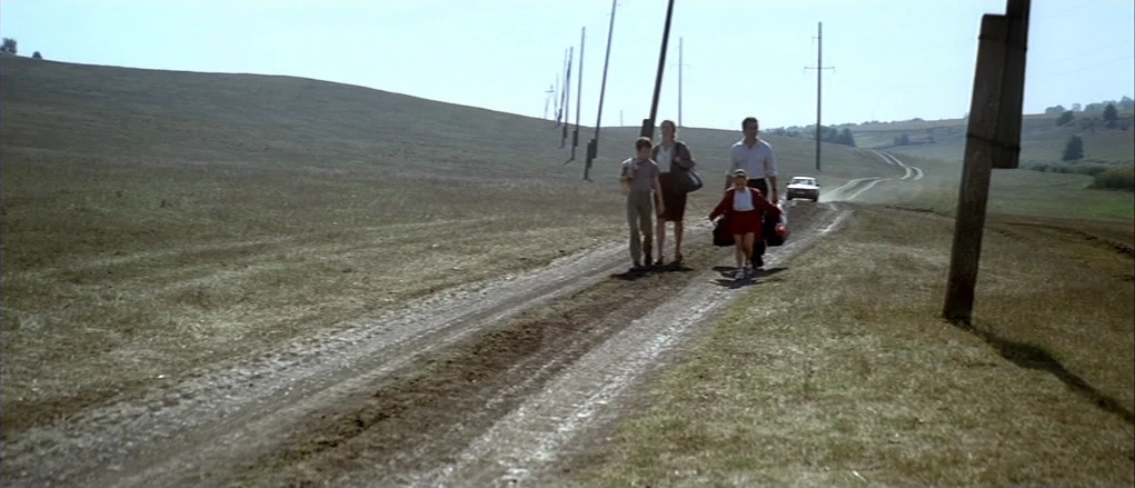 The Banishment (2007) movie still: wide — A group of four people walks down a dirt road in a vast field. Several utility poles follow the road as it…