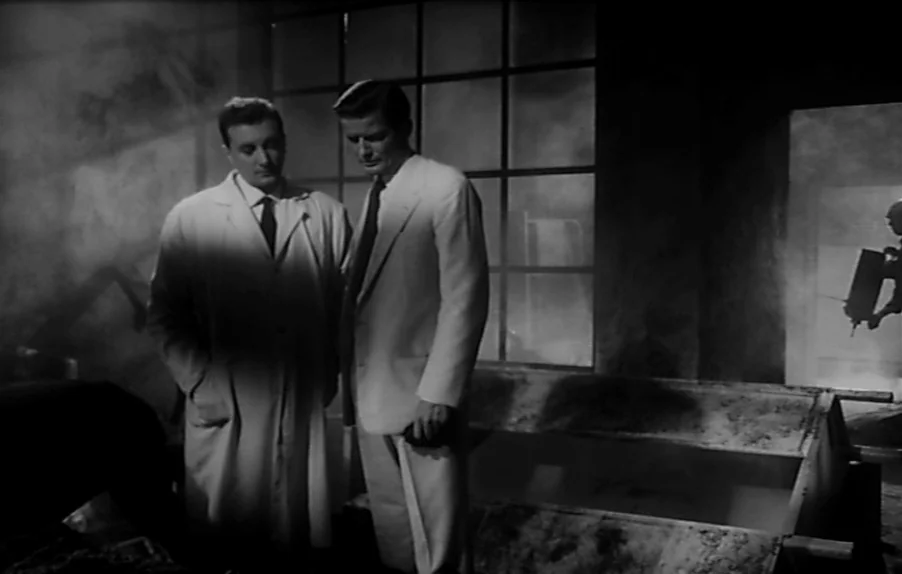 Caltiki, The Immortal Monster (1959) movie still: medium — A dark laboratory features a large metal vat and a grid-paned window filled with fog. Two…