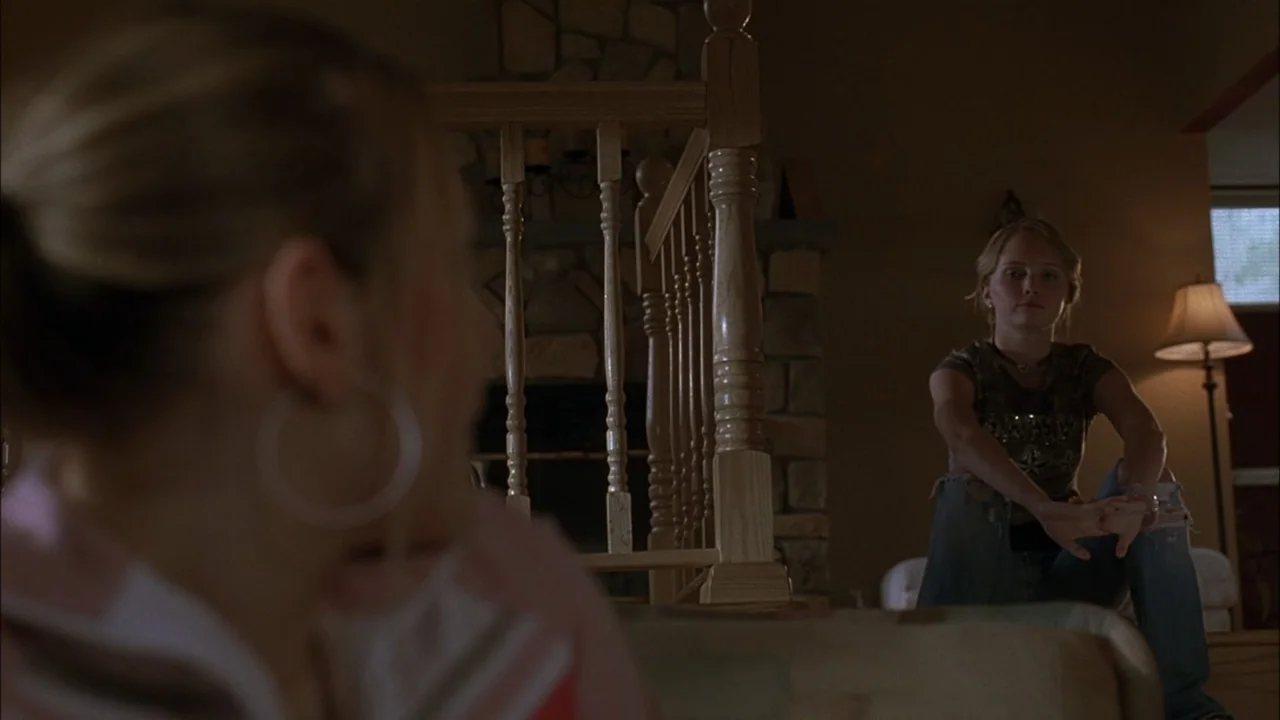 The Babysitters (2008) movie still: medium — A residential home interior features a stone fireplace, a wooden staircase, and warm lighting. Two…