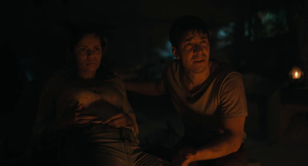 Barbarian (2022) movie still: medium — A dark, dimly lit room contains two figures huddled together in the low light. A man rests a hand on a…