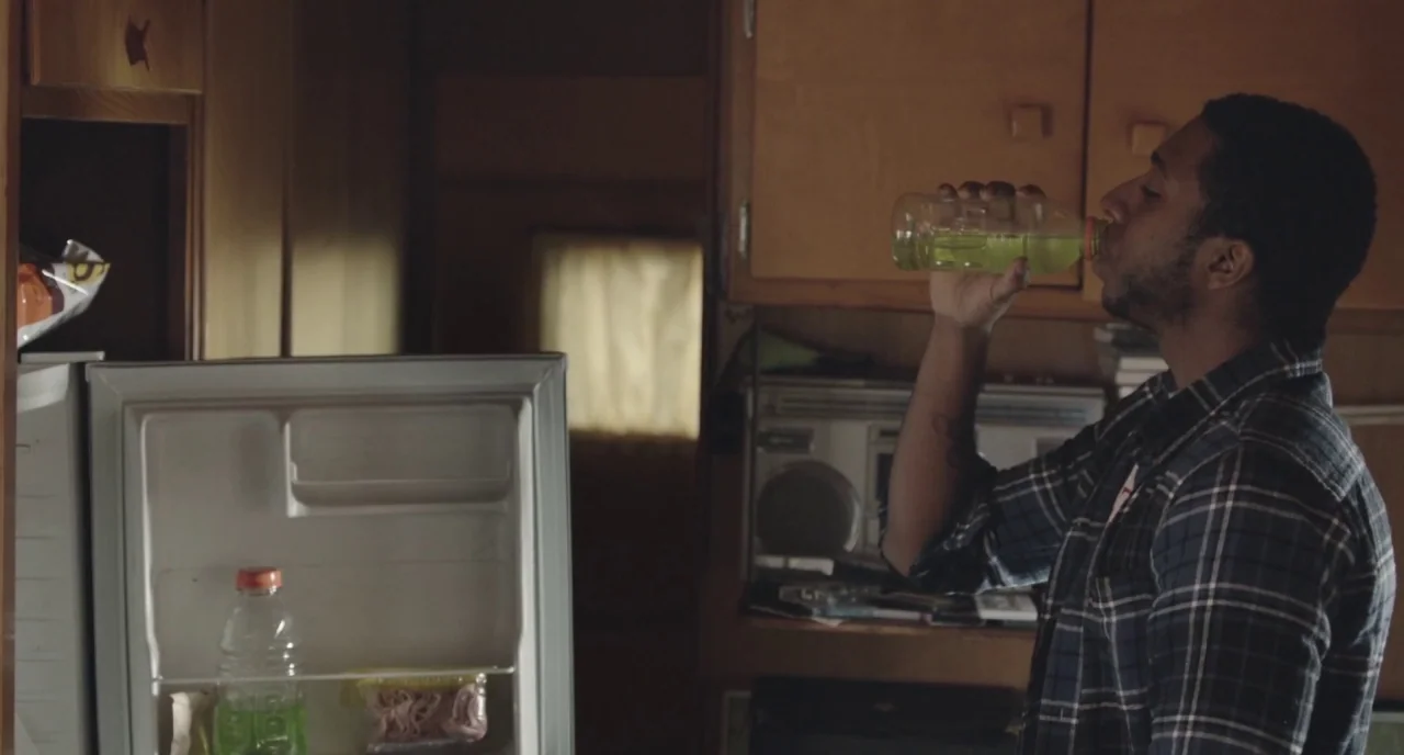 The Alchemist Cookbook (2016) movie still: medium — A modest kitchen with wooden cabinets and an open refrigerator. A young man stands in front of…