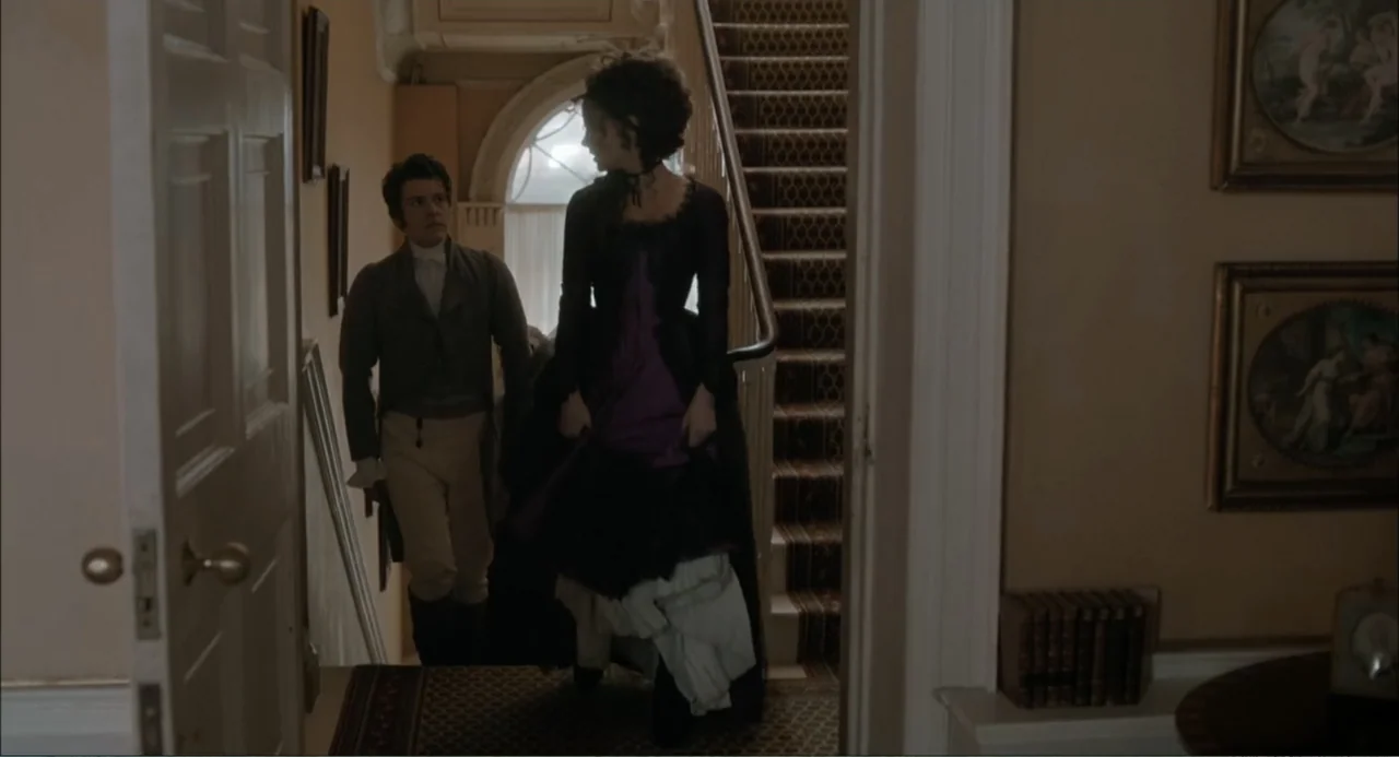 Love & Friendship (2016) movie still: fullbody — A historic residential staircase features ornate wallpaper and framed artwork on the walls. A man…