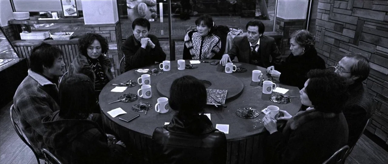 Lady Vengeance (2005) movie still: wide — A group of nine people sits around a circular table in a dining establishment. They appear to be engaged…