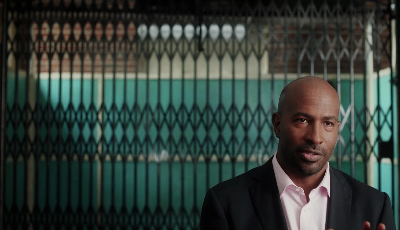 13th (2016) movie still: medium — A man stands in front of a vintage metal sliding gate inside a small space. The gate features a diamond-patterned…