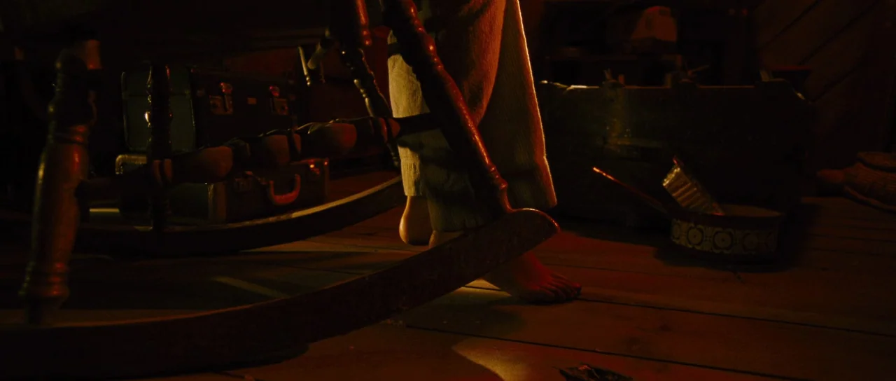 Black Christmas (2006) movie still: closeup — A dark wooden attic contains a rocking chair and old vintage suitcases. Dust motes dance in the amber…
