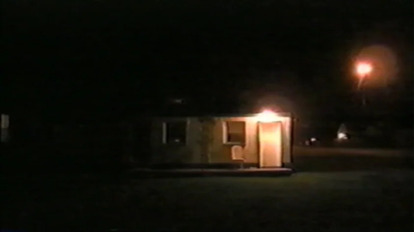 Trash Humpers (2009) movie still: wide — A small isolated structure sits in darkness with an open door at night. A lone streetlamp glows in the…