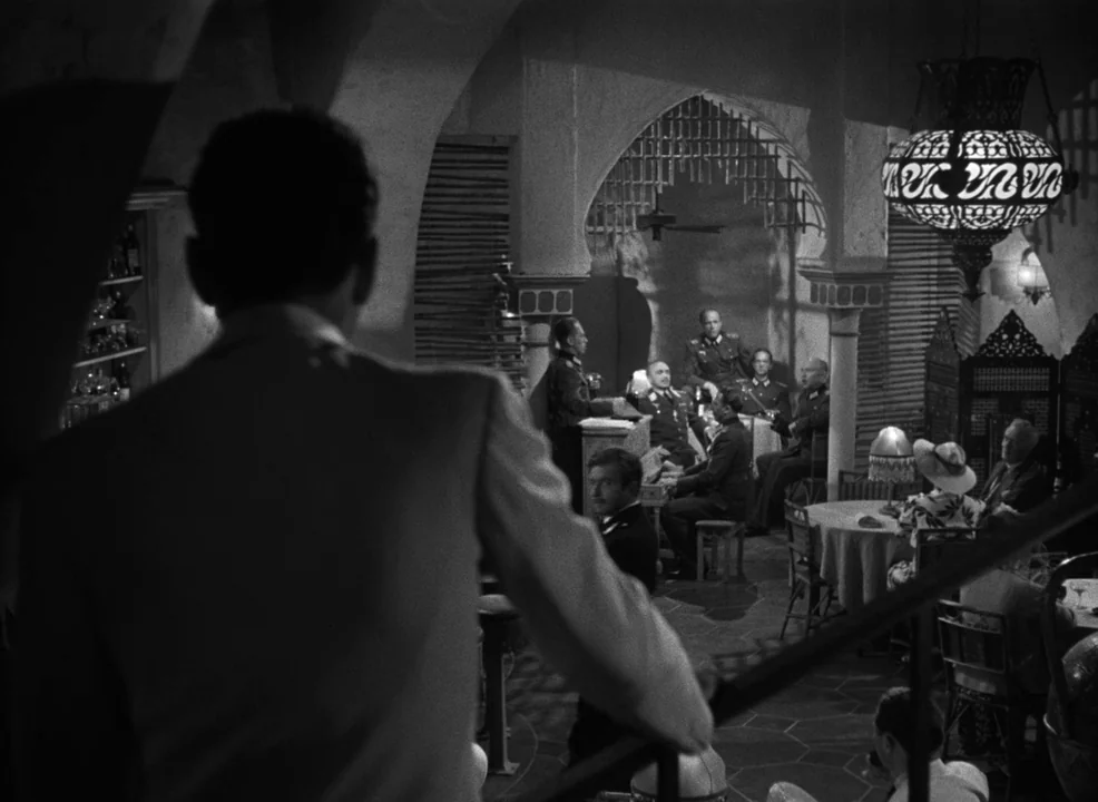 Casablanca (1942) movie still: medium — A dimly lit lounge with high arched ceilings and ornate hanging lamps. Several men in military uniforms sit…