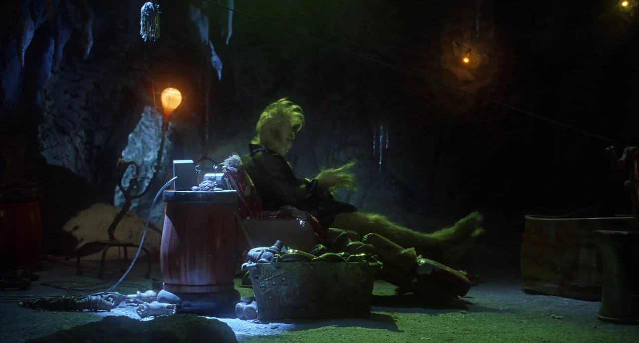 How The Grinch Stole Christmas (2000) movie still: wide — A dark rocky cavern contains a cluttered makeshift living space with discarded metal…