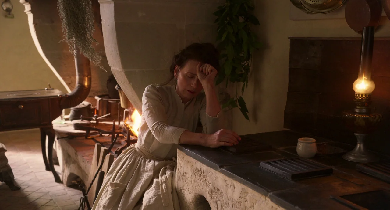 The Taste of Things (2023) movie still: medium — A rustic stone-built hearth area features an iron stove and hanging dried herbs. A woman in period…