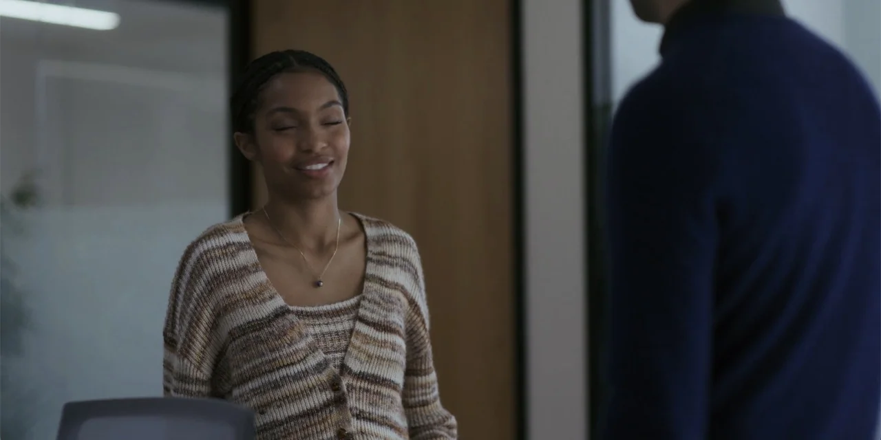 Sitting in Bars with Cake (2023) movie still: medium — A quiet office setting features a person in a knit sweater. The subject stands with her eyes…