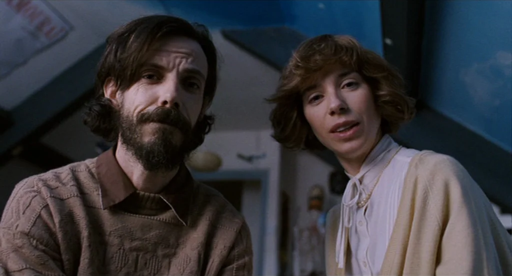 Submarine movie still: medium — An interior space featuring a man and woman looking downward at the camera. The background shows an angled ceiling…