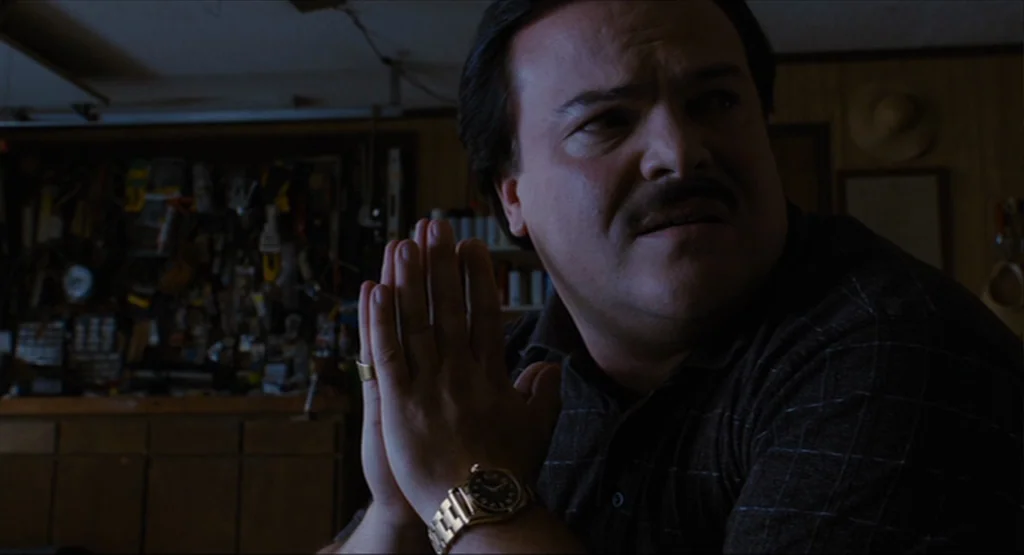 Bernie (2011) movie still: medium — A dark garage interior features a wall covered with numerous organized hand tools. A man in a patterned shirt…