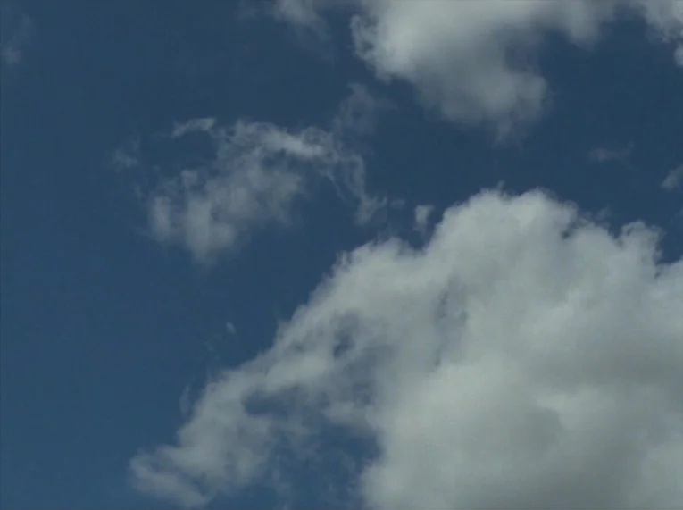 Keep Your Right Up (1987) movie still: establishing — A clear blue sky contains several white cumulus clouds distributed across the frame. Sunlight…