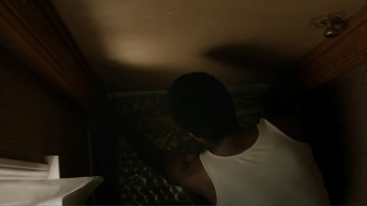 Nightingale (2014) movie still: medium — A dark, cramped residential closet interior with wooden walls and a metal door knob. A man in a white…