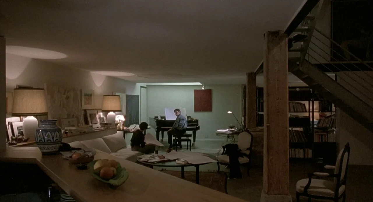 Three Colours: Blue (1993) movie still: wide — An open-plan loft space with wooden columns, a staircase, and varied antique furniture. A man plays…