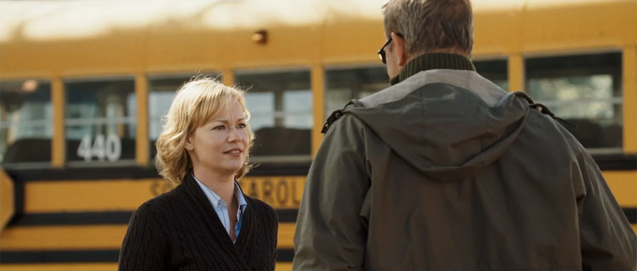 The New Daughter (2009) movie still: medium — A woman speaks to a man in front of a parked school bus. The scene occurs outdoors during the daytime…