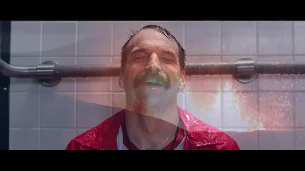 Collective: Unconscious (2016) movie still: closeup — A man stands in a brightly lit, sterile room with white tiled walls and exposed pipes. He…