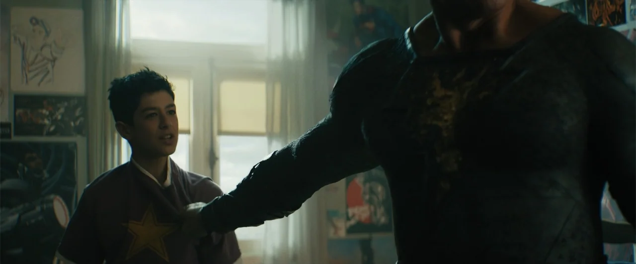 Black Adam (2022) movie still: medium — A bedroom contains walls covered with numerous posters and posters of fictional characters. A muscular…