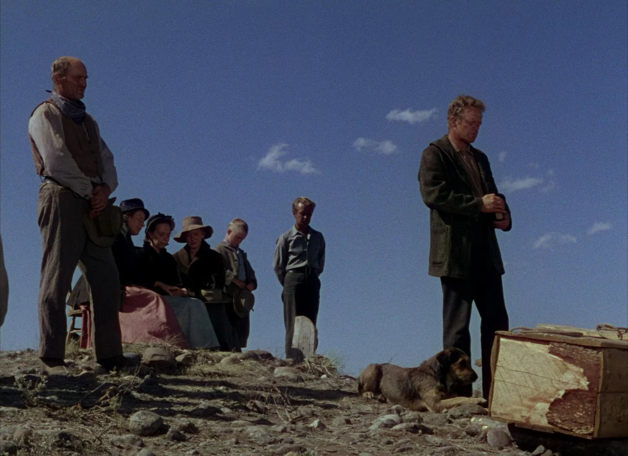 Shane (1953) movie still: fullbody — A rural gravesite on a desolate hilltop under a clear, bright blue sky. A group of mourning people stands near…