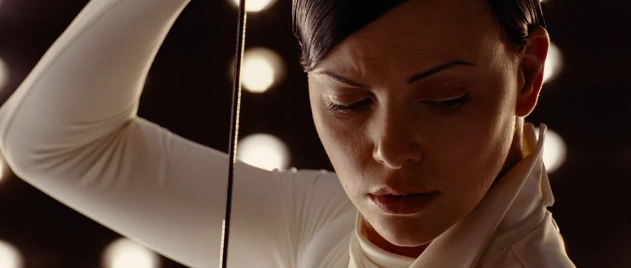 Aeon Flux (2005) movie still: closeup — A dark environment with blurred circular lights in the background. A woman in a white high-collared shirt…