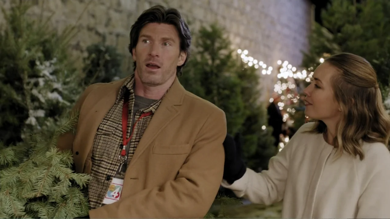 Peppermint and Postcards (2023) movie still: medium — A nighttime Christmas tree lot features rows of fir trees and glowing fairy lights. A man…