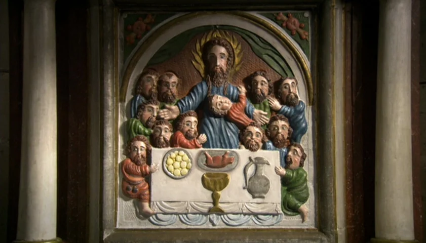 Saraband (2003) movie still: closeup — A painted wooden relief carving portrays figures gathered around a central table with food. The carving is…