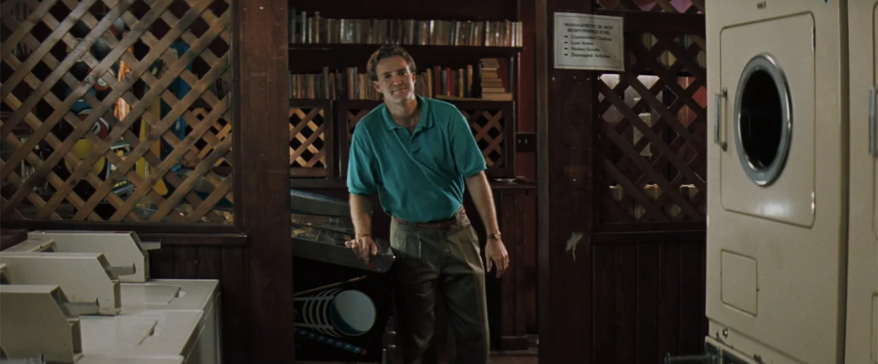 The Pelican Brief (1993) movie still: medium — A laundromat interior features wood-paneled walls with lattice dividers and a pinball machine. A man…