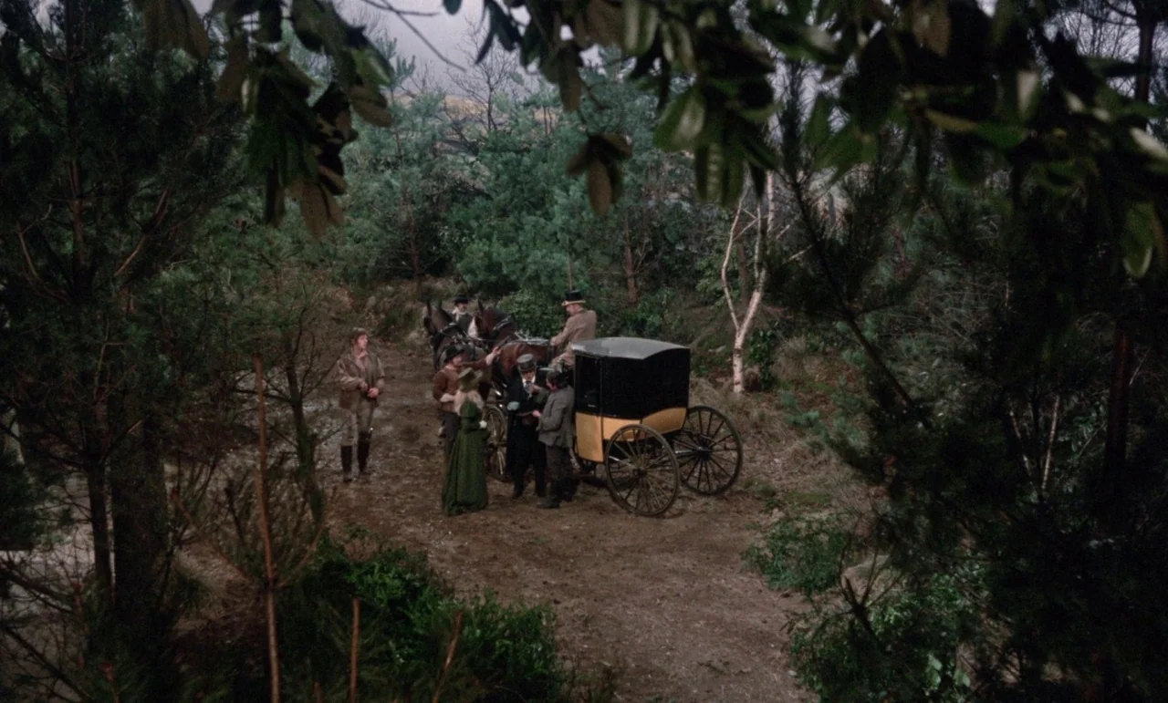 The Horror of Frankenstein (1970) movie still: wide — A group of people in Victorian attire congregates on a muddy dirt road. They stand near a…