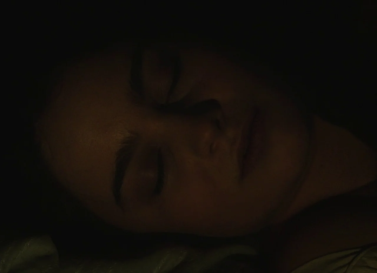 The Nightingale (2018) movie still: closeup — A dark bedroom at night with only a sliver of ambient light visible. A person lies sleeping with their…