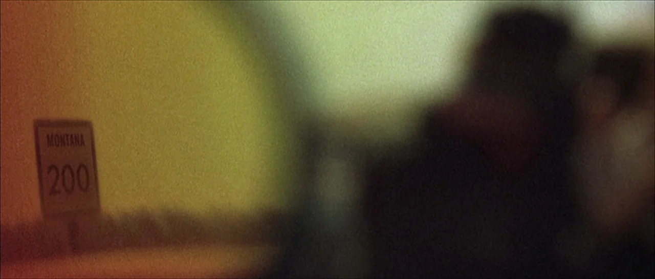 Fear X (2003) movie still: wide — A roadside sign indicating Montana 200 sits on the left side of the frame. The background is a heavily blurred,…