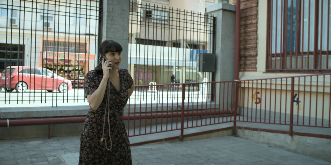 The Three Wise Men: The Truth (2022) movie still: medium — A woman stands on a concrete sidewalk in front of a metal security fence. She is speaking…