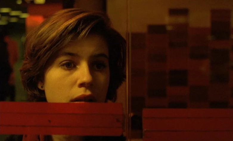 The Double Life of Véronique (1991) movie still: closeup — A woman looks through a glass door marked with a bold horizontal red stripe. The…