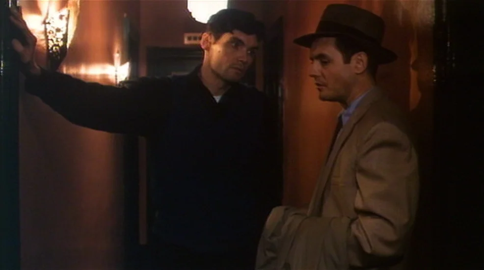 Union City (1980) movie still: medium — A dimly lit narrow corridor features wood-paneled walls and a single glowing wall sconce. Two men in…