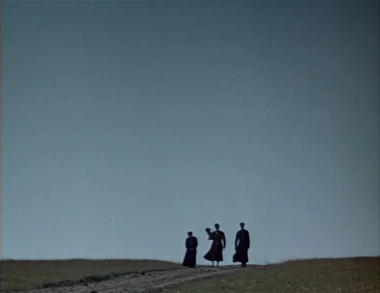 Viy (1967) movie still: wide — A desolate grassy hillside under an expansive, overcast gray sky. Three figures in dark clothing walk away from the…