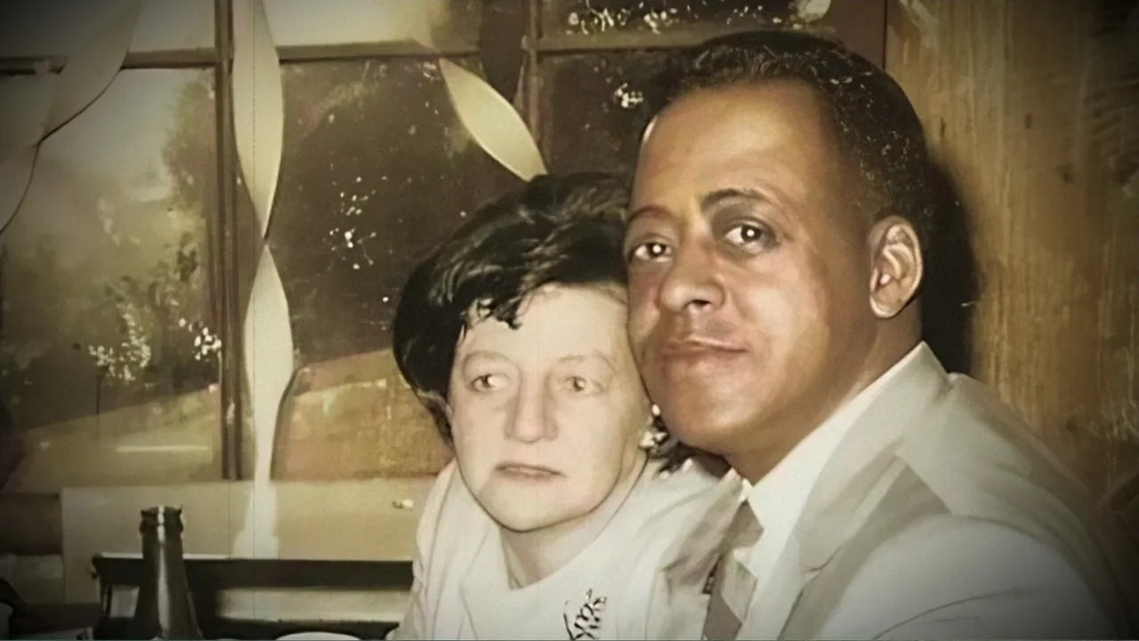 Alien Abduction: Betty and Barney Hill (2022) movie still: closeup — A vintage 1960s photograph depicts a couple seated at a table indoors. A man…