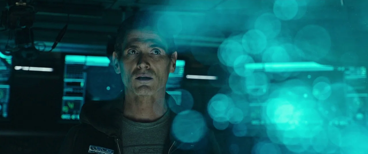 Alien: Covenant (2017) movie still: medium — A dark, cramped command console interior bathed in harsh, flickering neon teal light. A middle-aged man…