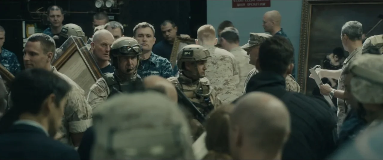 World War Z (2013) movie still: medium — A crowded interior space contains many individuals in military camouflage and plain clothing. The group…