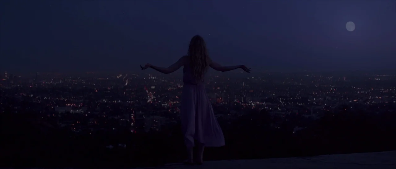 The Neon Demon (2016) movie still: fullbody — A high-altitude overlook provides a view of a sprawling city at night. A young woman stands at the…