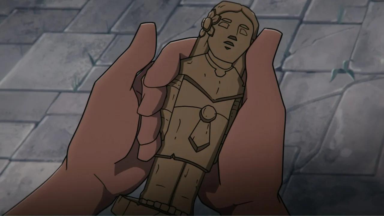 Aztec Batman: Clash of Empires (2025) movie still: closeup — A pair of hands holds a carved wooden figurine against a stone tiled ground. The…