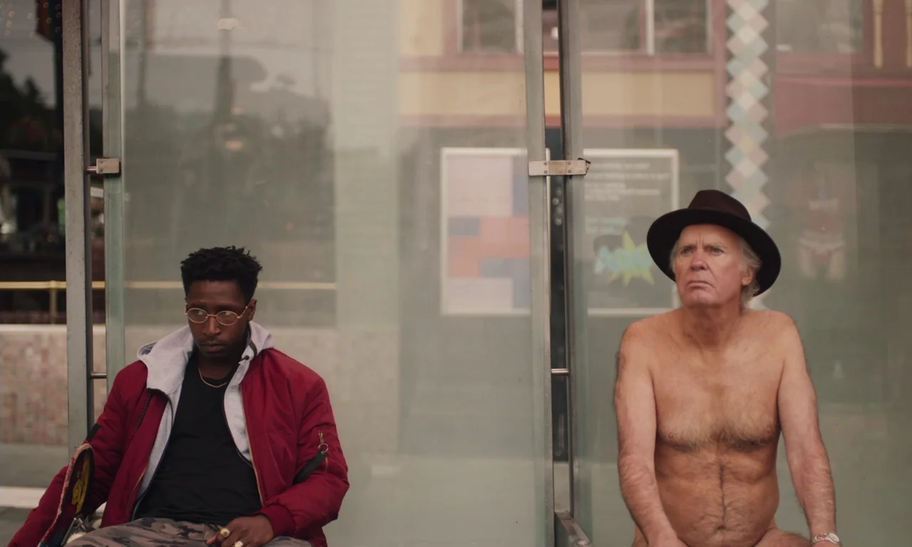 The Last Black Man in San Francisco (2019) movie still: medium — A glass-walled bus stop enclosure sits on a paved city sidewalk. A young man and an…