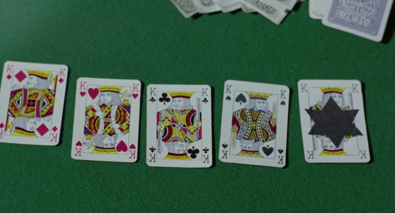 Johnny Colt (1966) movie still: closeup — Five playing cards featuring kings are arranged horizontally on a green felt table surface. Several blurry…