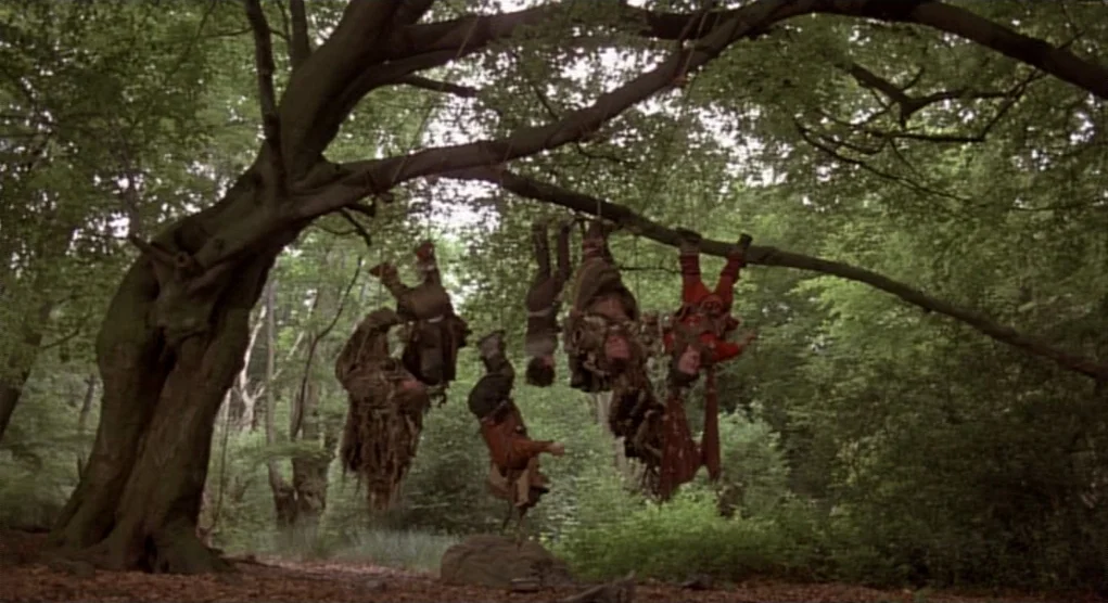 Time Bandits (1981) movie still: wide — A cluster of fantasy-style characters hang upside down from a large, sturdy tree branch. Ropes are tied…
